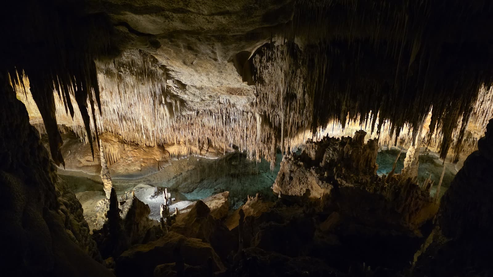 Blankytně modr&eacute; podzemn&iacute; jezero v Drač&iacute;ch jeskyn&iacute;ch pod hustou clonou stalaktitů